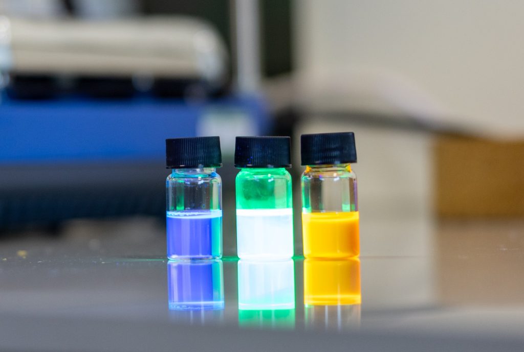 Image of 3 multicoloured and lightly glowing vials with blue, green/white and yellow liquids.