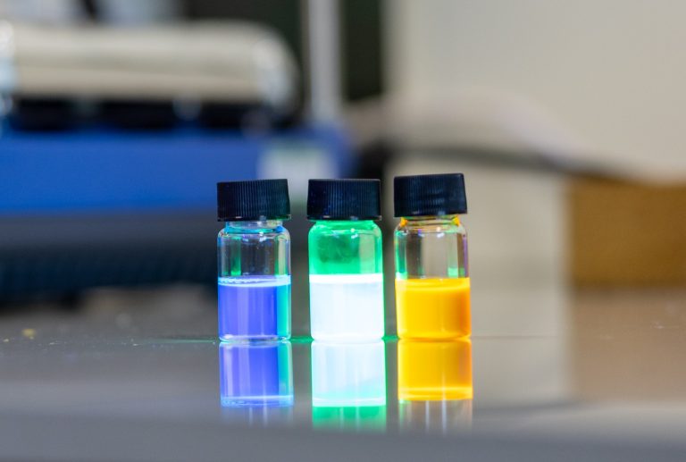 Image of 3 multicoloured and lightly glowing vials with blue, green/white and yellow liquids.