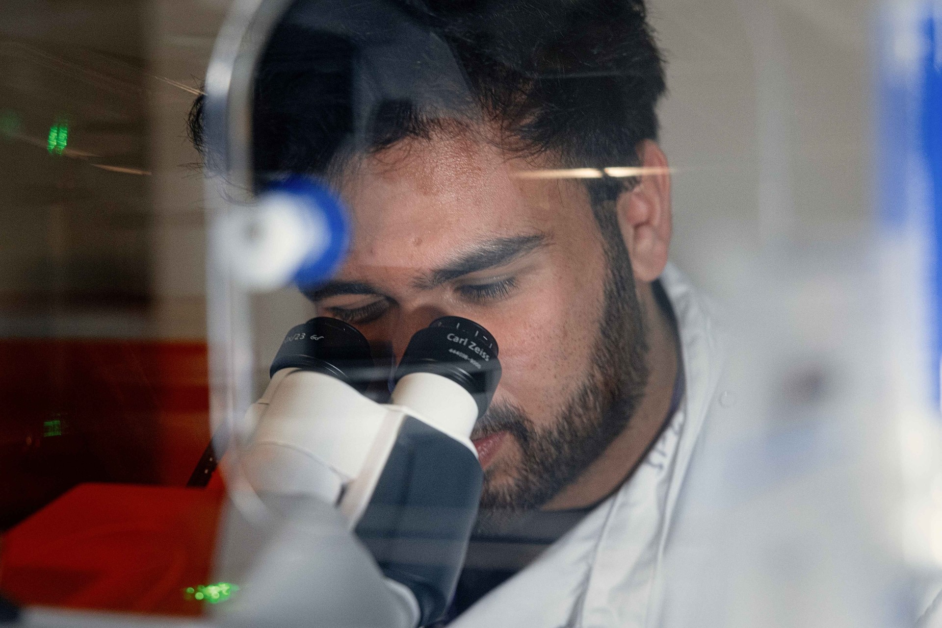 Male researcher in lab coat looks down microscope lens.