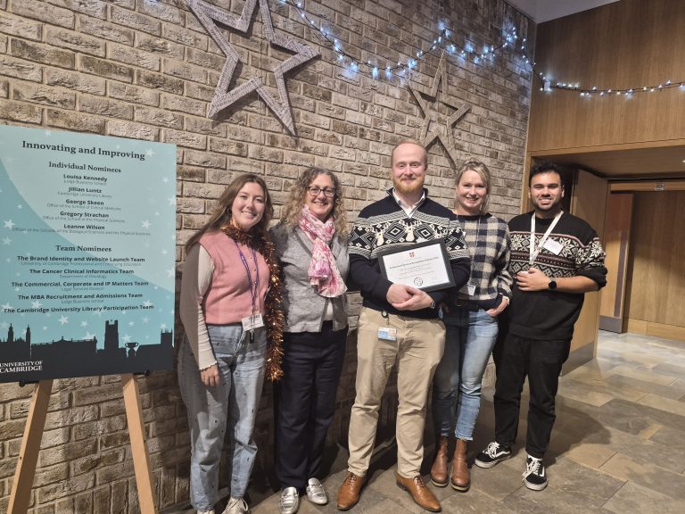 Four people surround Alex Carvell who holds his winning certificate smiling at the camera.
