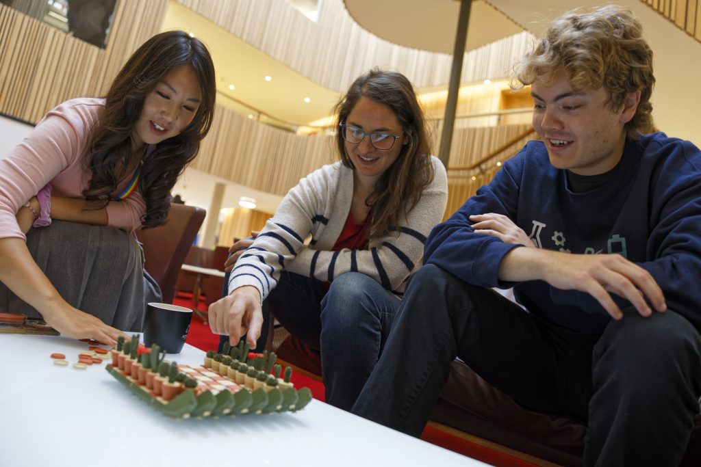 Three people play chess in relaxed setting.