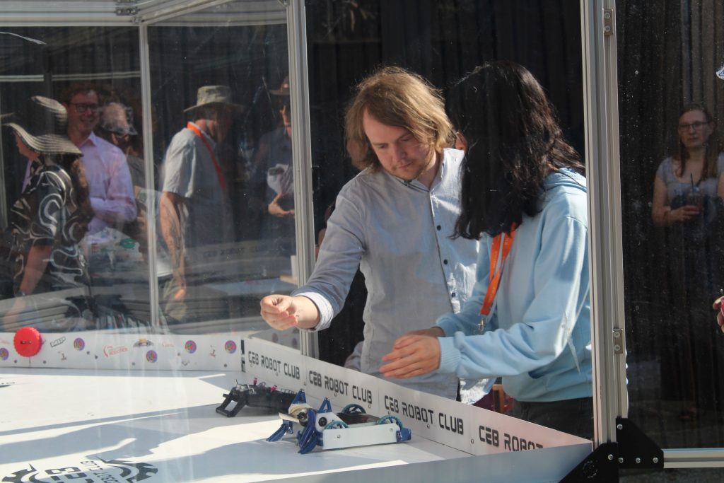 Man and woman work on small robot in pyrex case during robot club tournament.