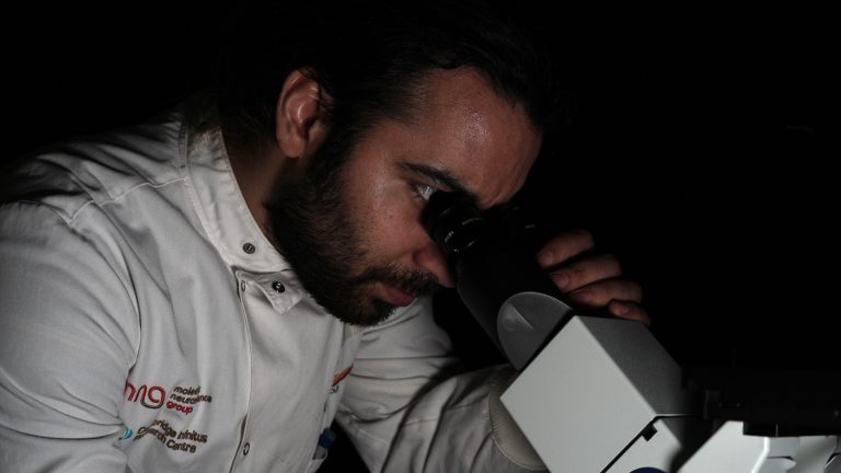 A male scientist peers into a microscope in a darkened lab