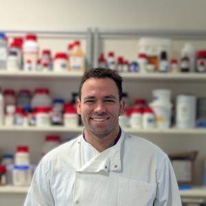 Portrait of a man in a lab coat. A lab environment forms the background.
