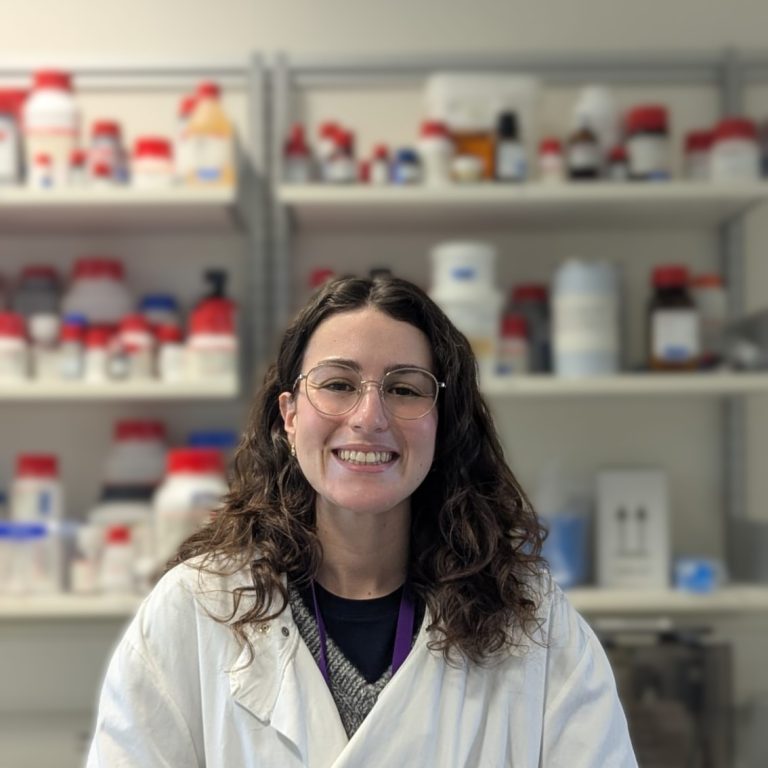 Portrait of a woman in a lab coat smiling at the camera. A lab forms the background.