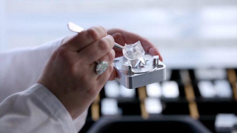 Hand in white lab coat holds tweezers with heart valve prototype.