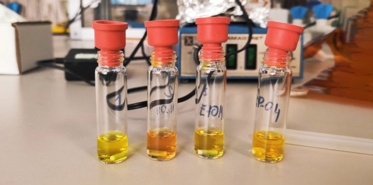four tubes of yellow liquid sitting on a laboratory workbench