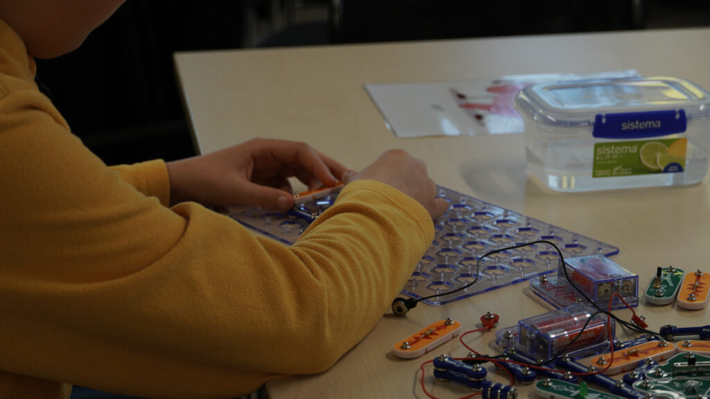 Small hands in yellow jumper play with electrical looking kit.