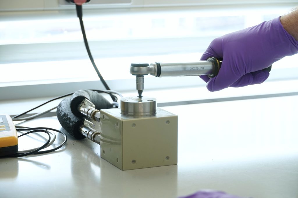 A hand wearing a purple nitrile glove uses a wrench